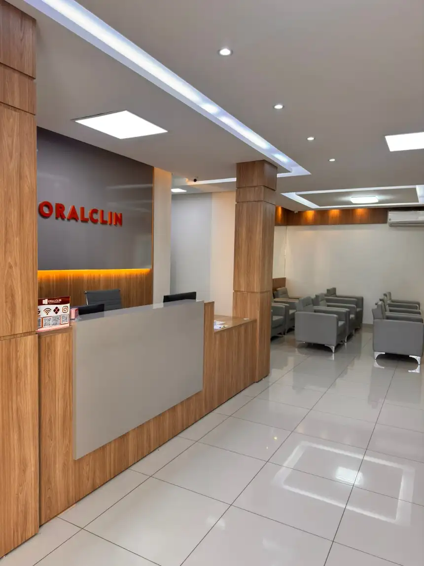 Recepção da OralClin: balcão de madeira clara, logotipo na parede e poltronas cinza na sala de espera.
